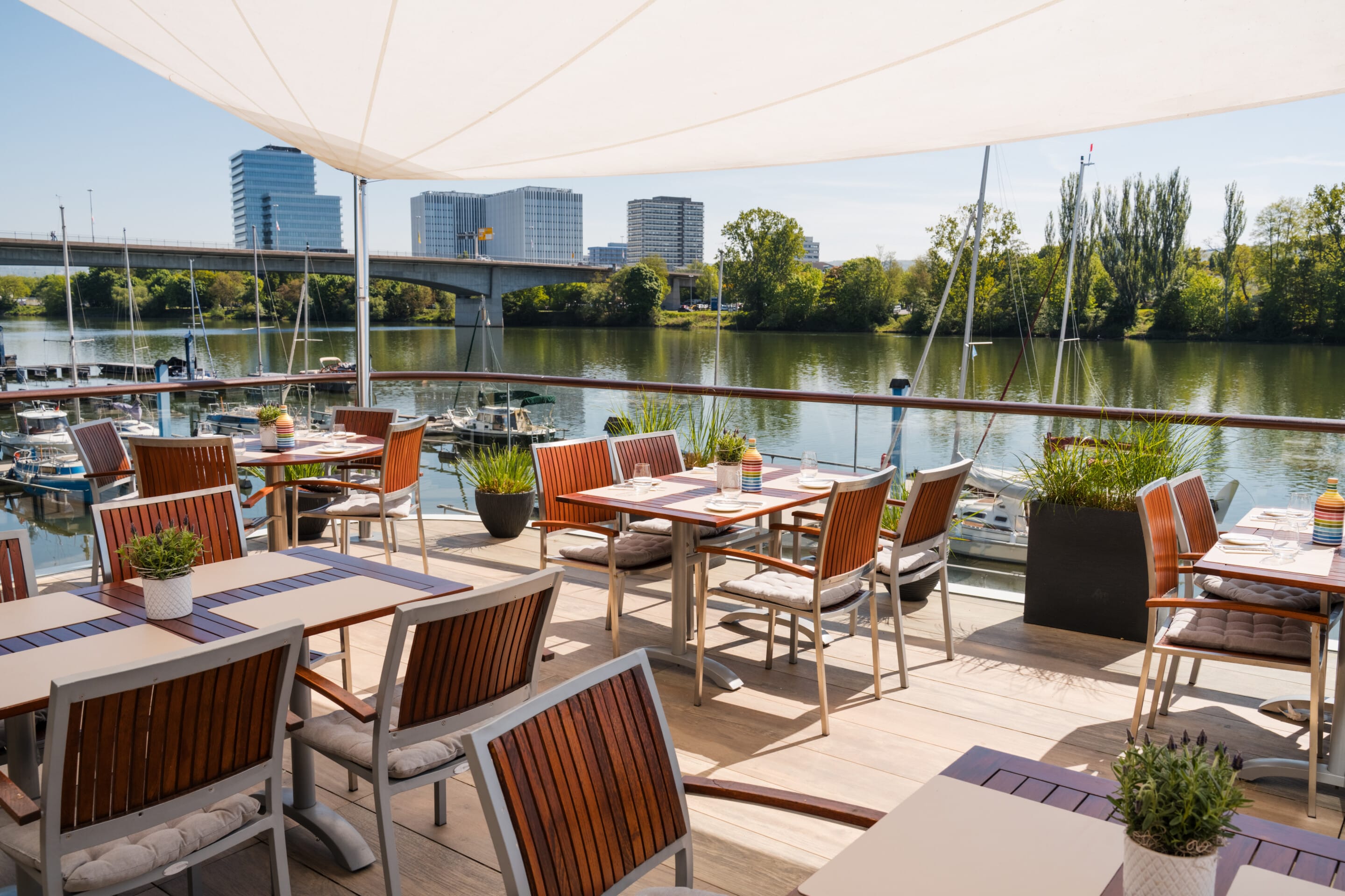 Gedeckte Tische unter weißen Sonnenschirmen auf der Restaurantterrasse des FÄHRHAUS Koblenz mit Blick auf die Mosel.